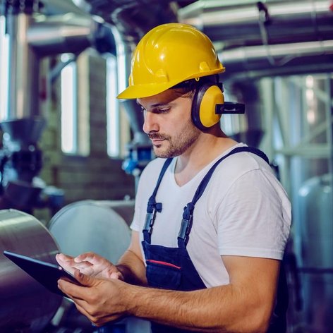 Ein Mann mit Bauhelm steht mit einem Tablet in einem Rohrraum